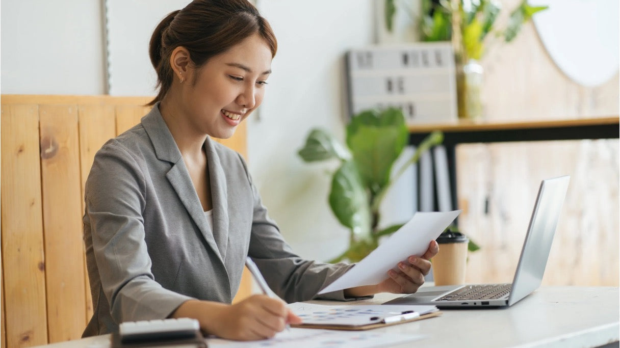 A smiling virtual assistant managing content tasks remotely, reviewing documents alongside a laptop in a bright workspace