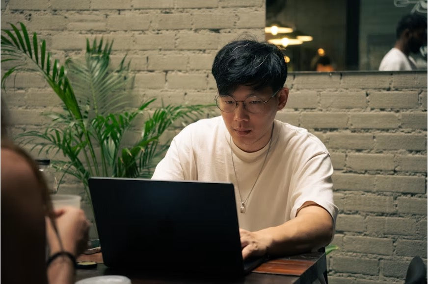 A male virtual assistant using a laptop in a workspace with a potted plant nearby