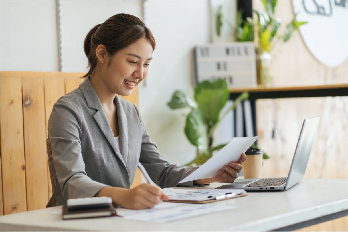 A smiling virtual assistant managing content tasks remotely, reviewing documents alongside a laptop in a bright workspace