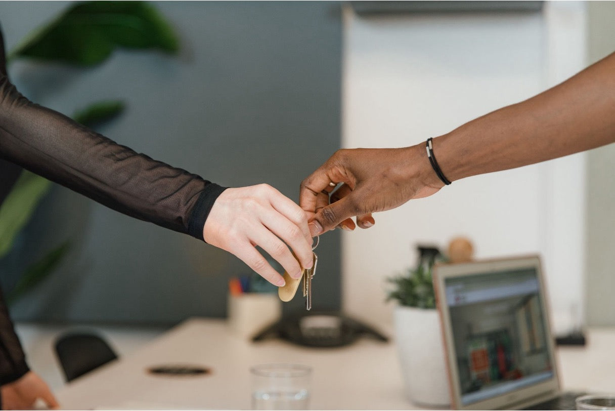 Two people exchanging a set of keys across an office desk with a laptop in the background.