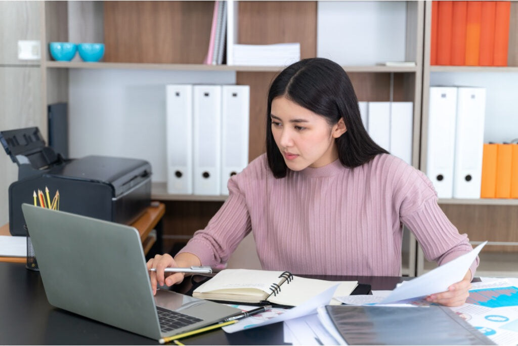 Virtual assistant preparing business documents while reviewing reports beside a laptop