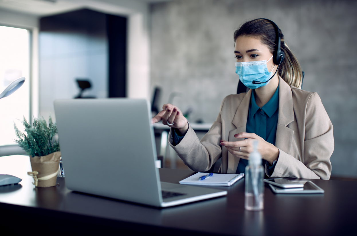 Virtual assistant wearing a face mask and headset handling client calls remotely from a professional office desk