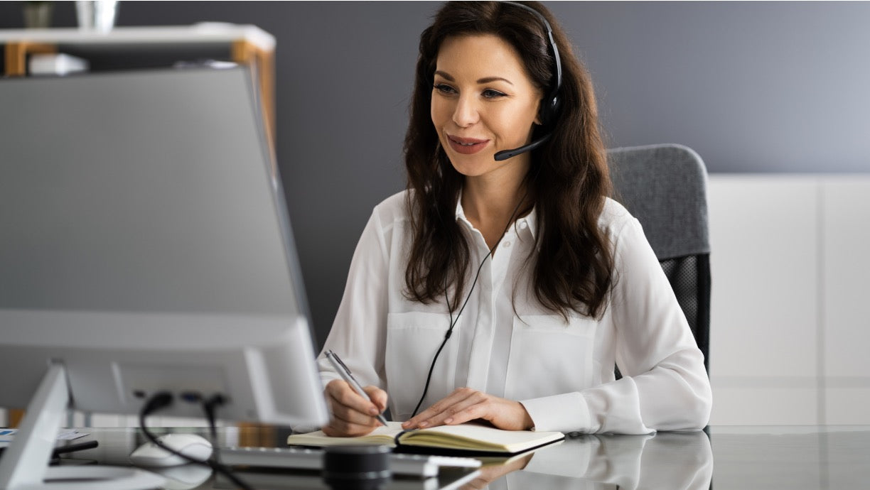  Virtual assistant wearing a headset and taking notes while managing tasks at a desktop computer
