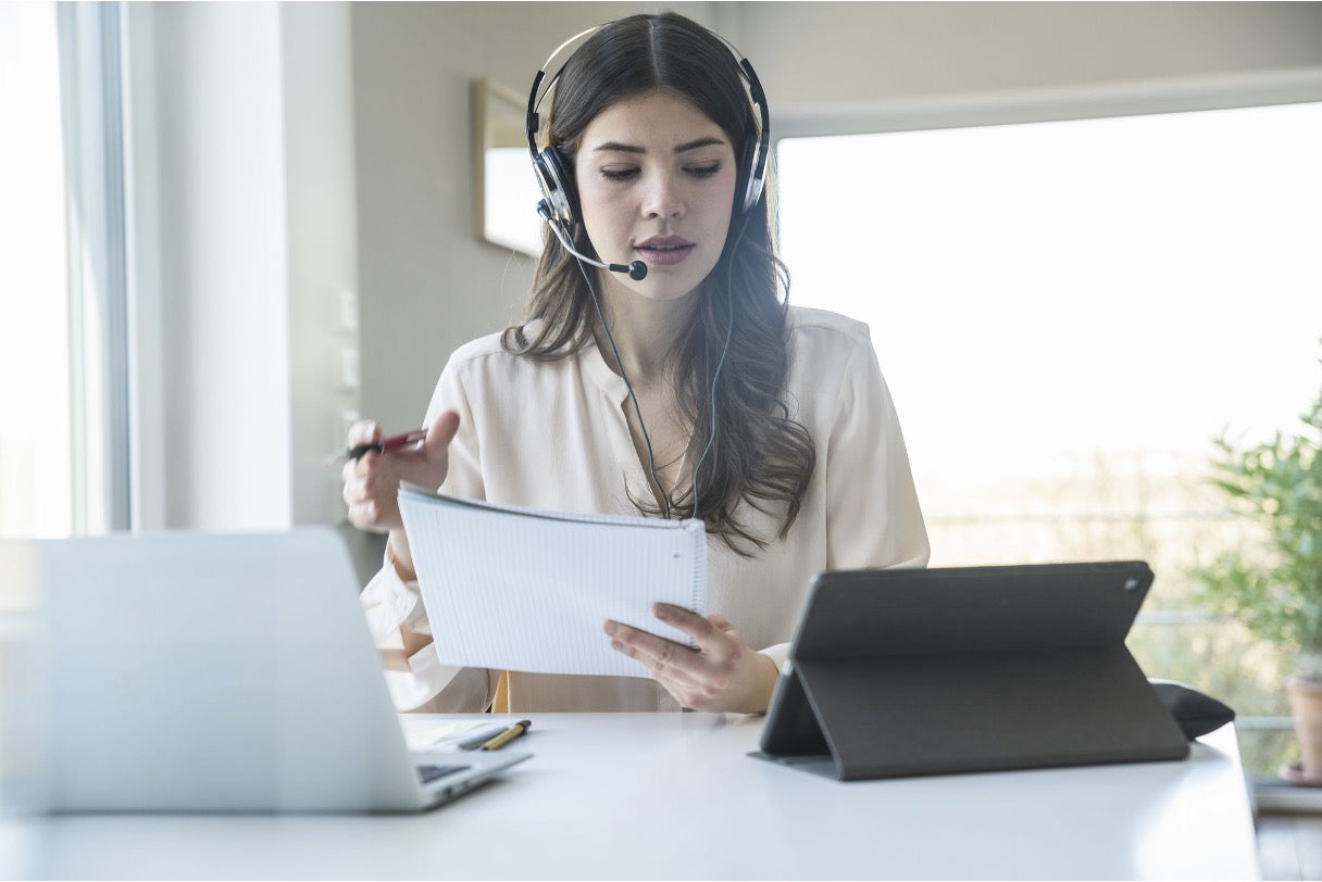 Virtual assistant wearing a headset manages appointments using a laptop, tablet, and notebook