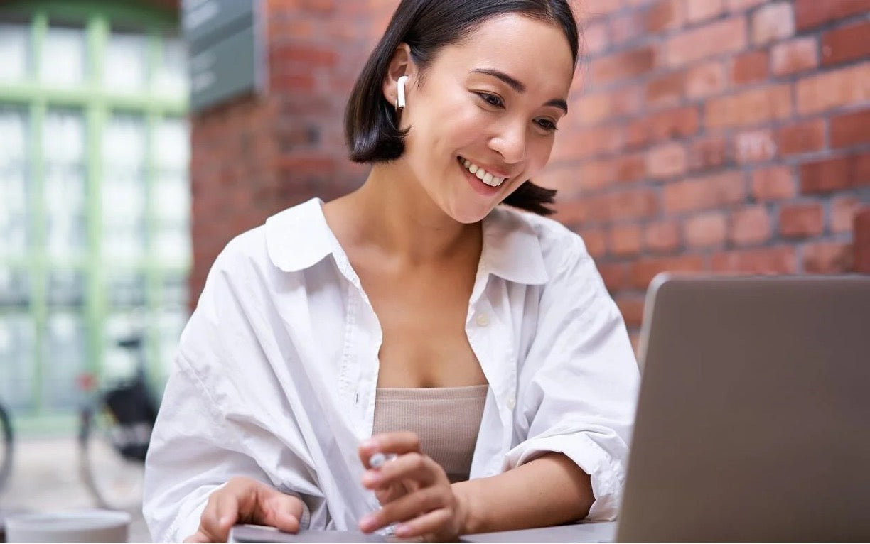 Woman with wireless earbuds managing emails on a laptop, representing a virtual assistant at work